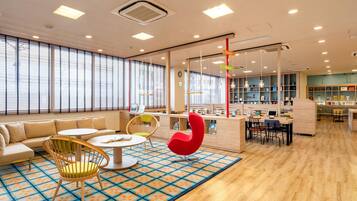 A modern library with a central reading area, individual study tables, and a large window with blinds.