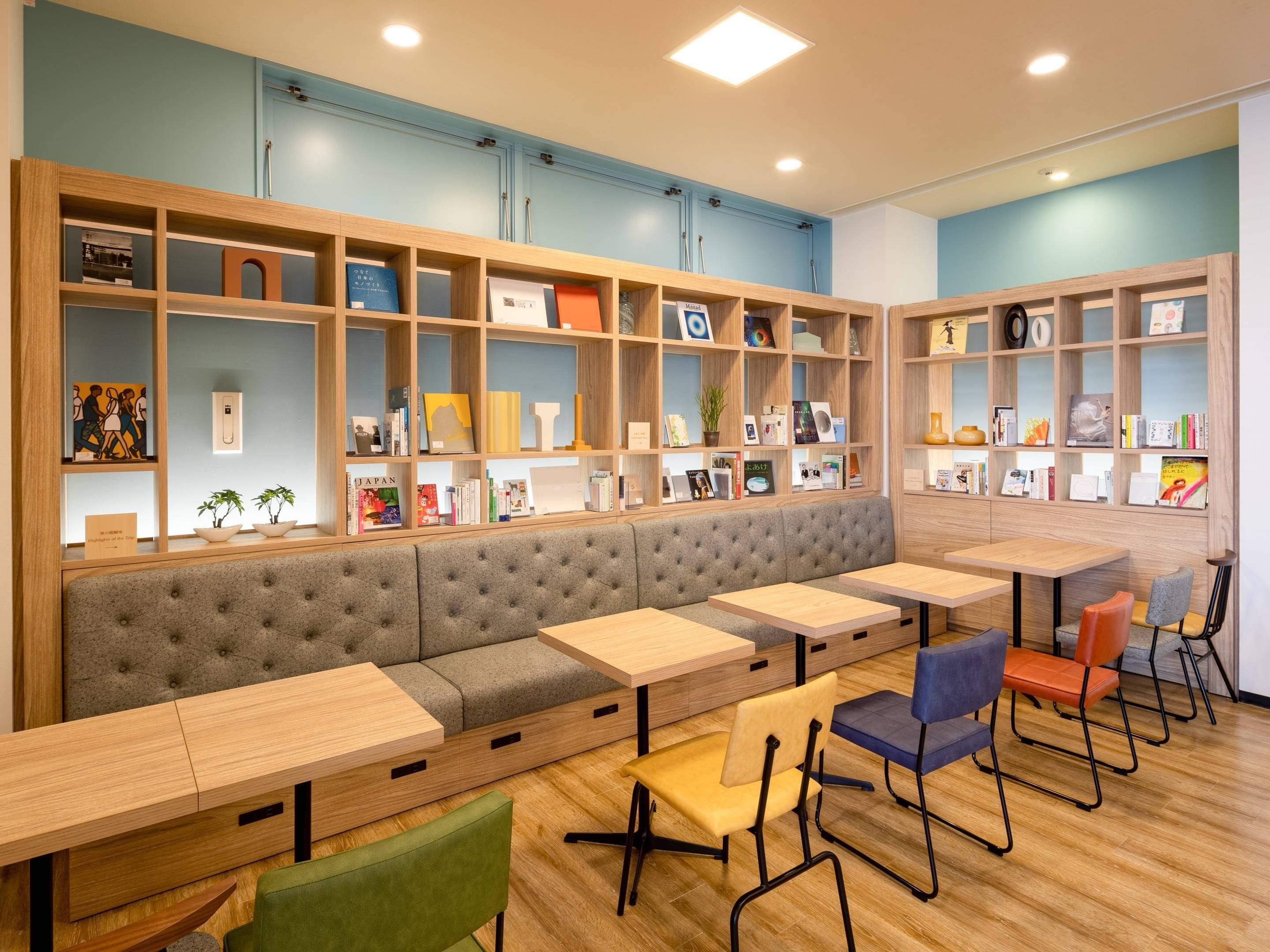 A modern library with a long bench, multiple tables, and bookshelves filled with books and decorative items.