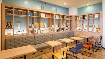 A modern library with a long bench, multiple tables, and bookshelves filled with books and decorative items.