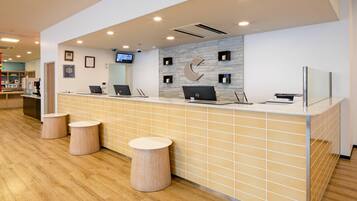 A reception area with a counter, two laptops, a TV, and three stools.