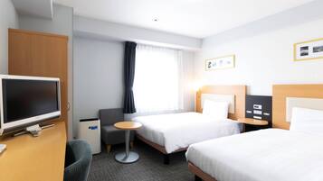 A hotel room with two beds, a desk with a flat-screen TV, a small round table, and a grey armchair.