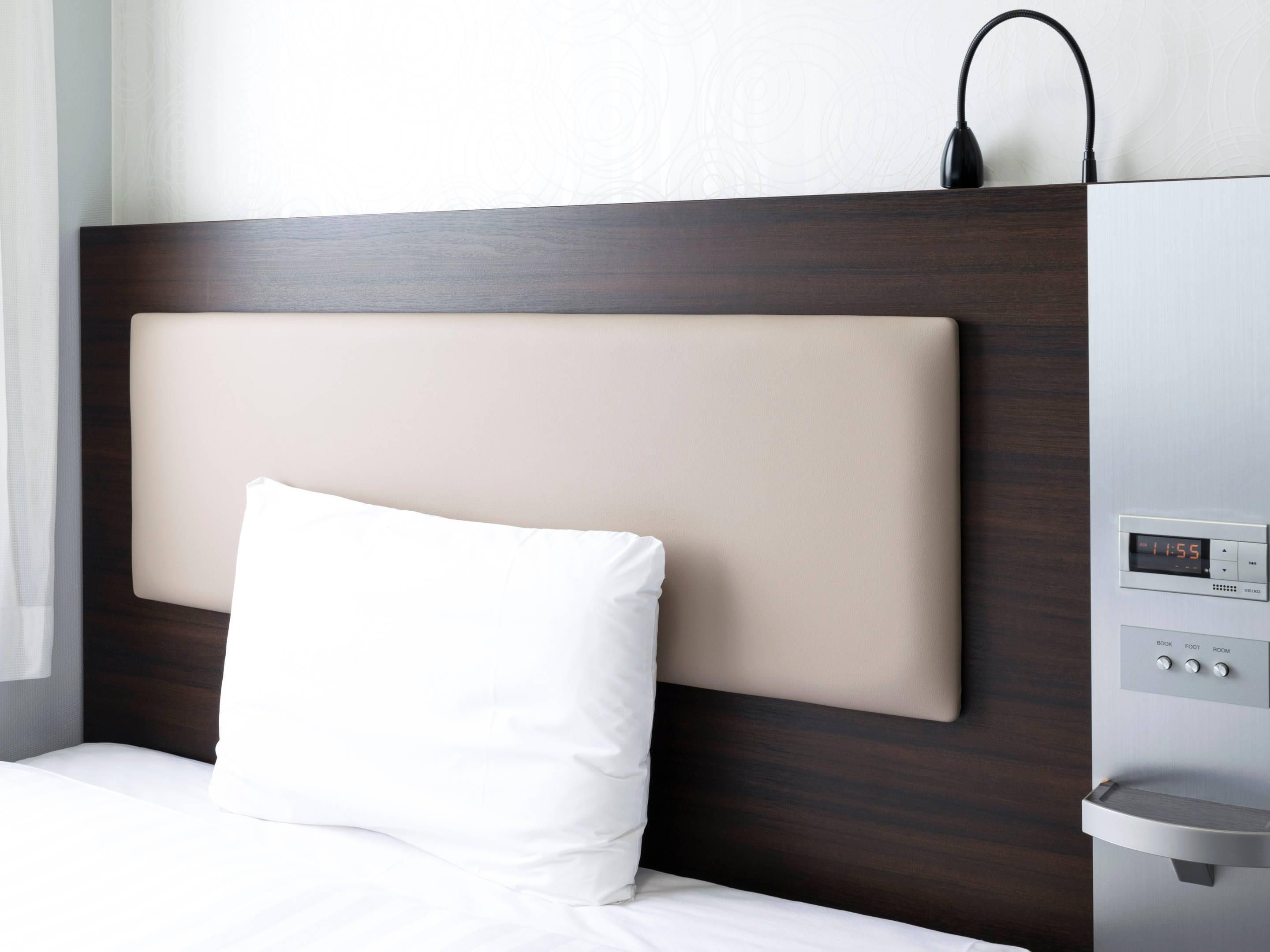 Una habitación de hotel con una cama moderna, un reloj digital y un panel de control para la configuración de la estancia.