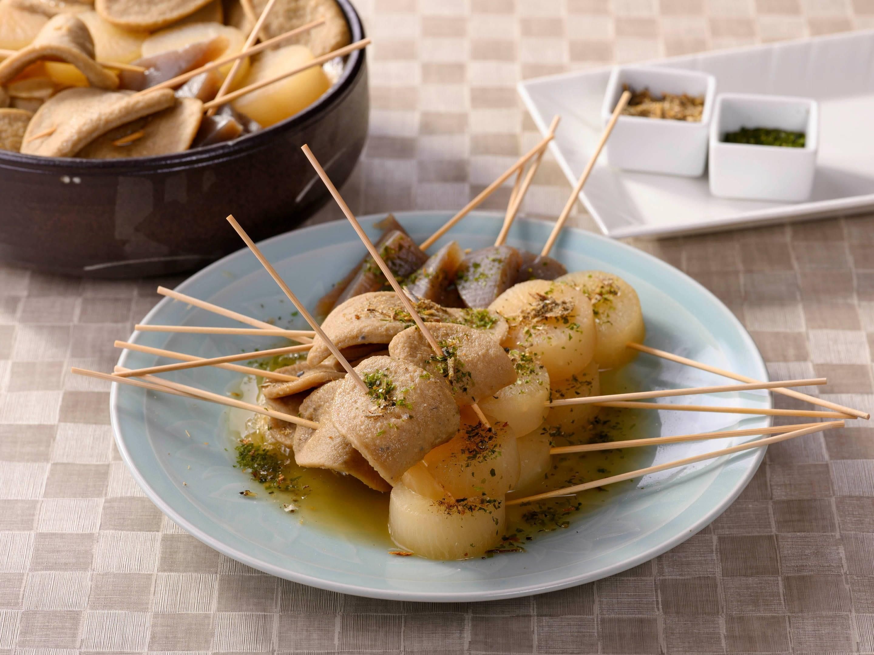 Prato com espetinhos e ervas, acompanhado de uma tigela e pequenos pratos ao fundo.