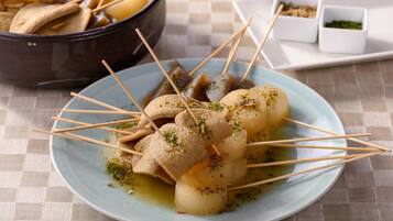 Prato com espetinhos e ervas, acompanhado de uma tigela e pequenos pratos ao fundo.