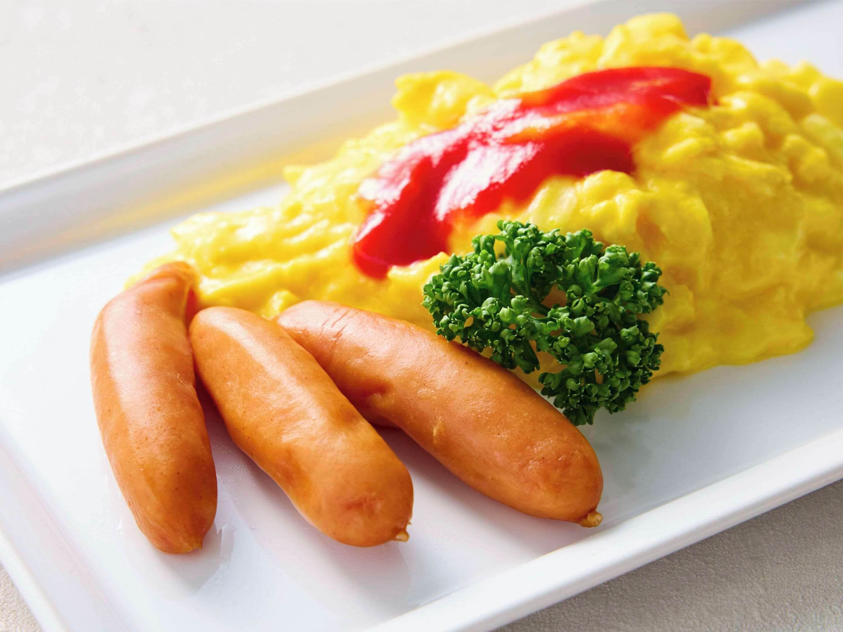 Un plato con huevos revueltos, salchichas y un poco de brócoli.