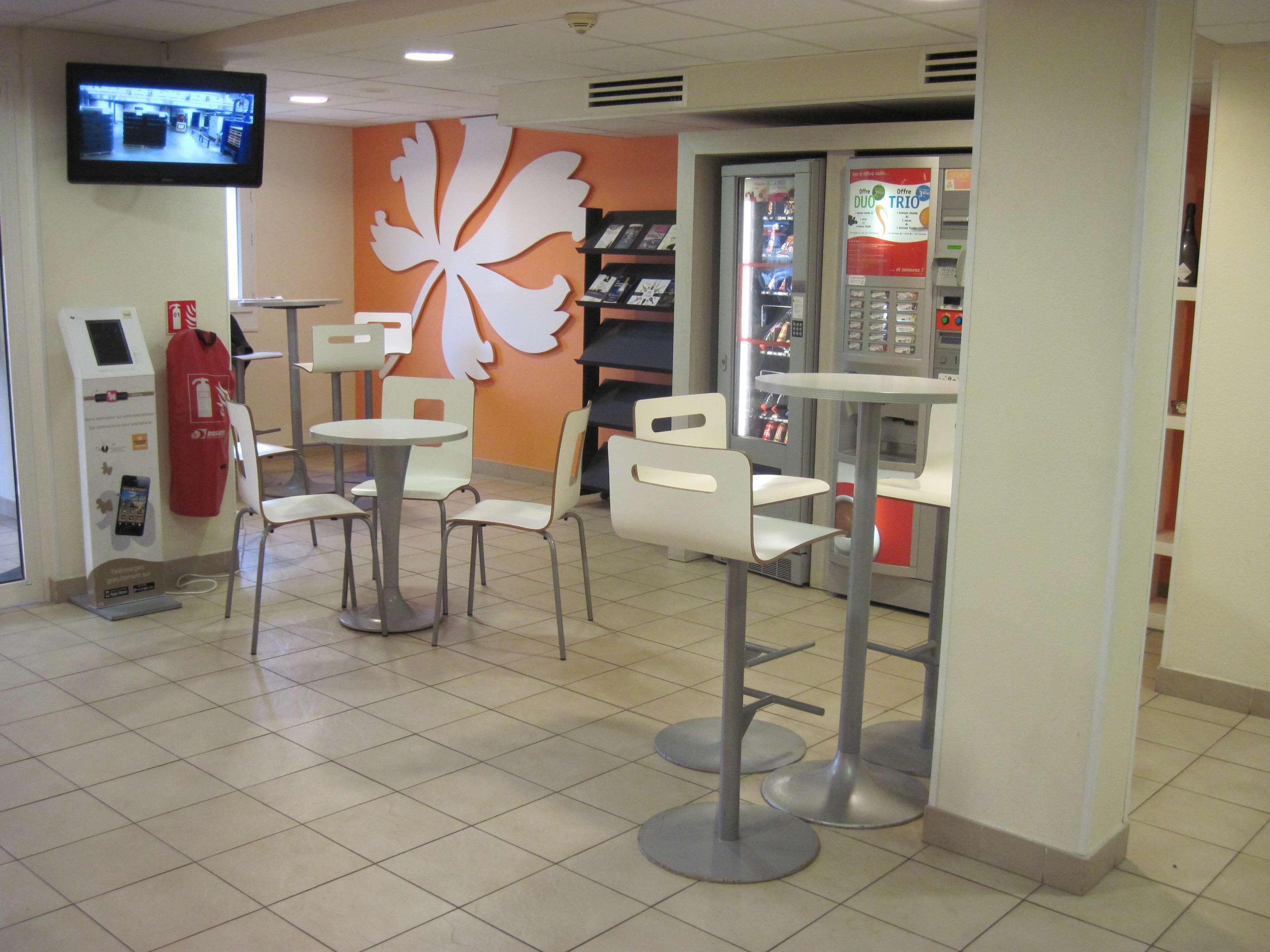 Interior de un restaurante de comida rápida con mesas, una máquina expendedora de bebidas y un televisor montado en la pared.