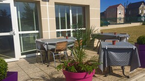 An outdoor patio area with tables and chairs, a potted plant, and a building with large windows and a door. - Premiere Classe Epernay (Epernay)