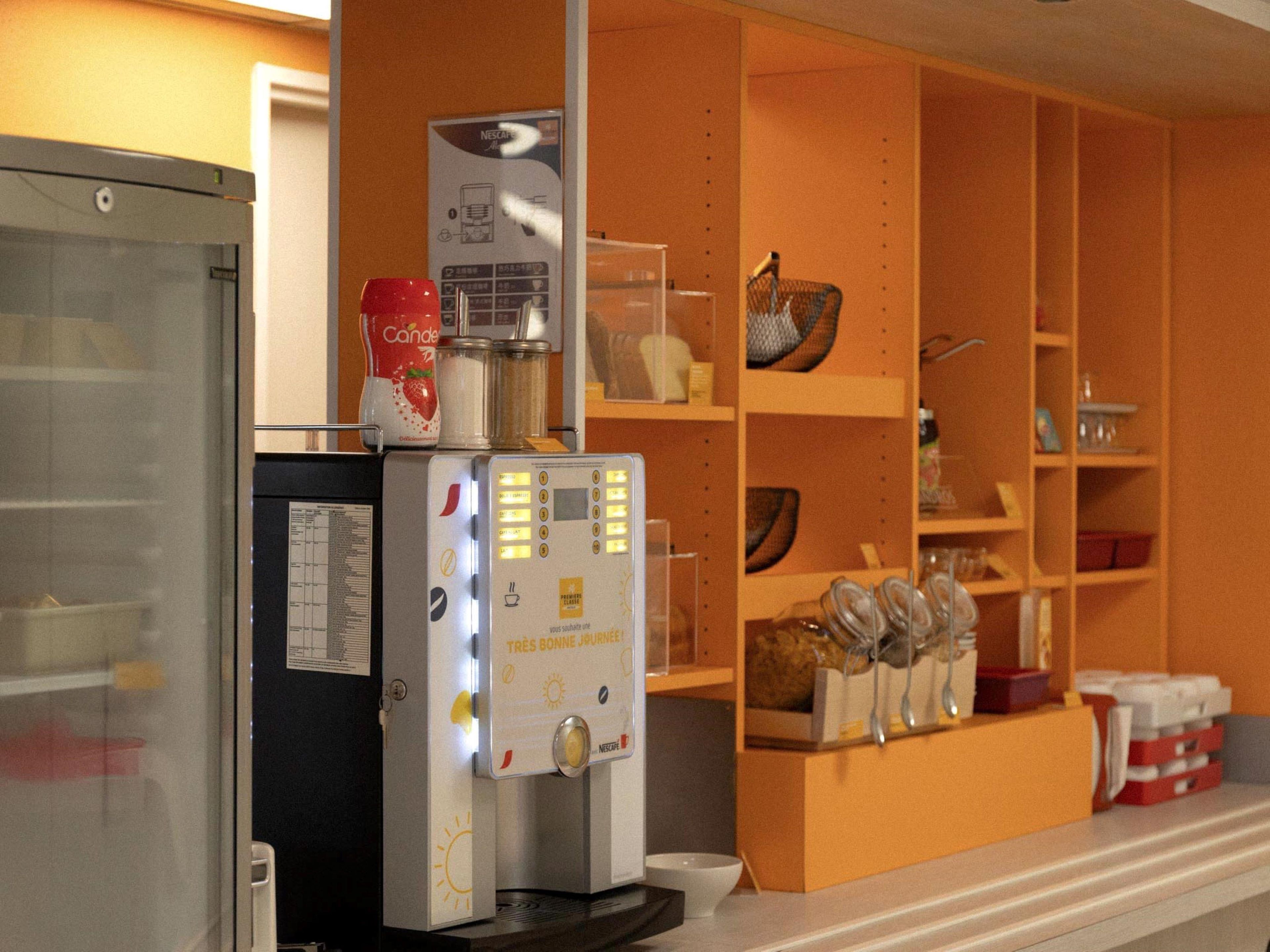 A kitchen area with a coffee machine, a refrigerator, and shelves with kitchenware.