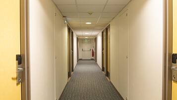 Un pasillo de hotel con pisos alfombrados, puertas a ambos lados y un extintor de incendios montado en la pared.