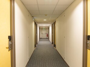 Un pasillo de hotel con pisos alfombrados, puertas a ambos lados y un extintor de incendios montado en la pared.
