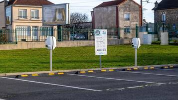 Un área de estacionamiento con estaciones de carga para vehículos eléctricos, un cartel y un edificio al fondo.
