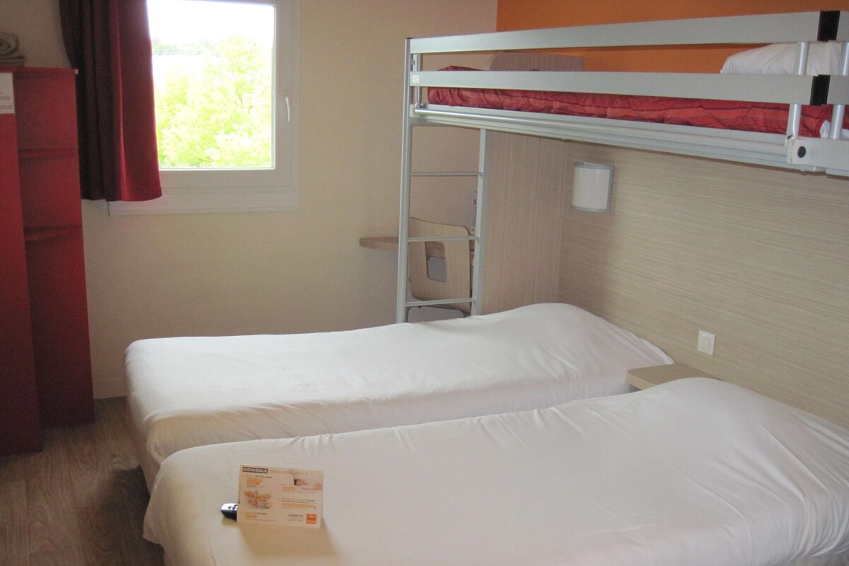 A room with two single beds, a small desk, a red cabinet, and a window with curtains.