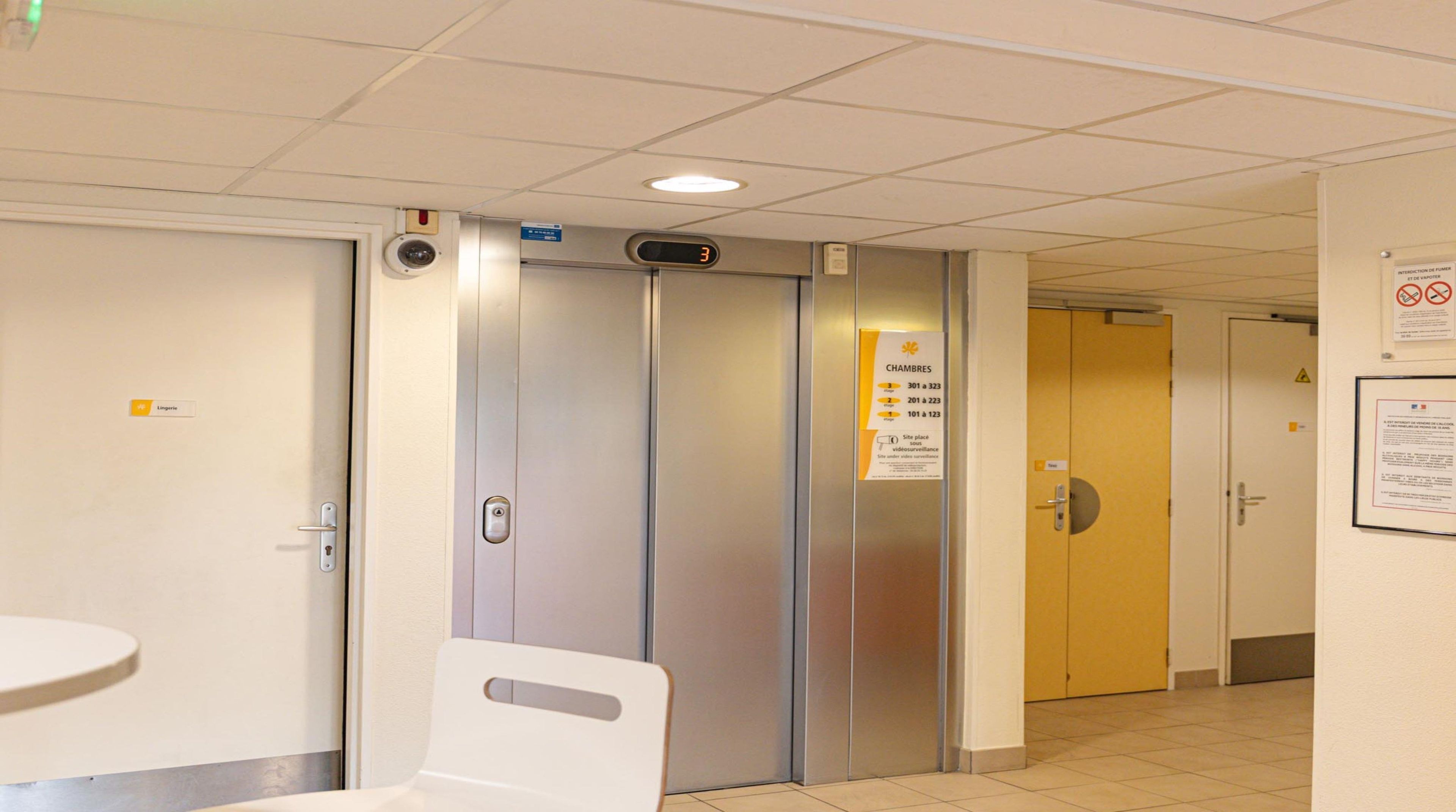 A hotel corridor with a closed elevator, a door labeled 'Lingerie,' and a sign indicating room numbers 301 to 323.