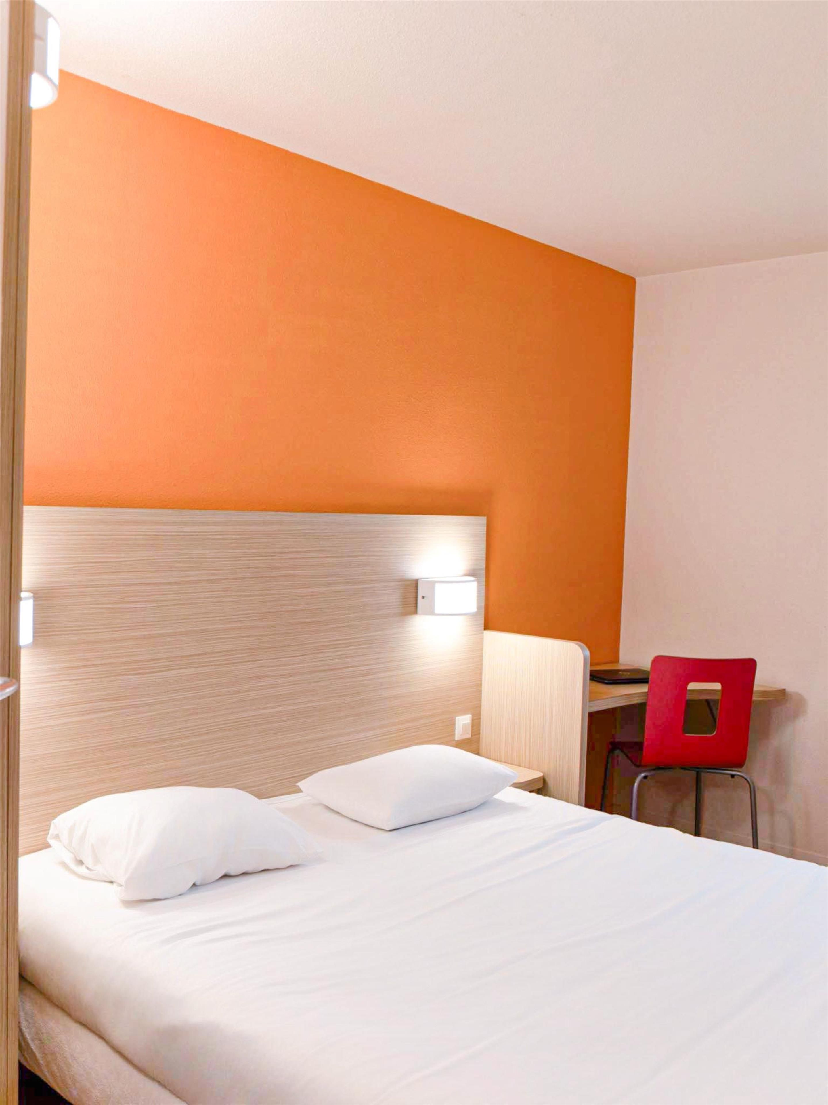 A hotel room with a bed, a desk, and a red chair.