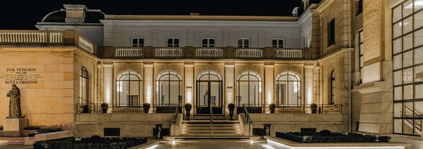 Un edificio imponente con una fachada simétrica, amplias ventanas en arco y una escalera central que conduce a un balcón.