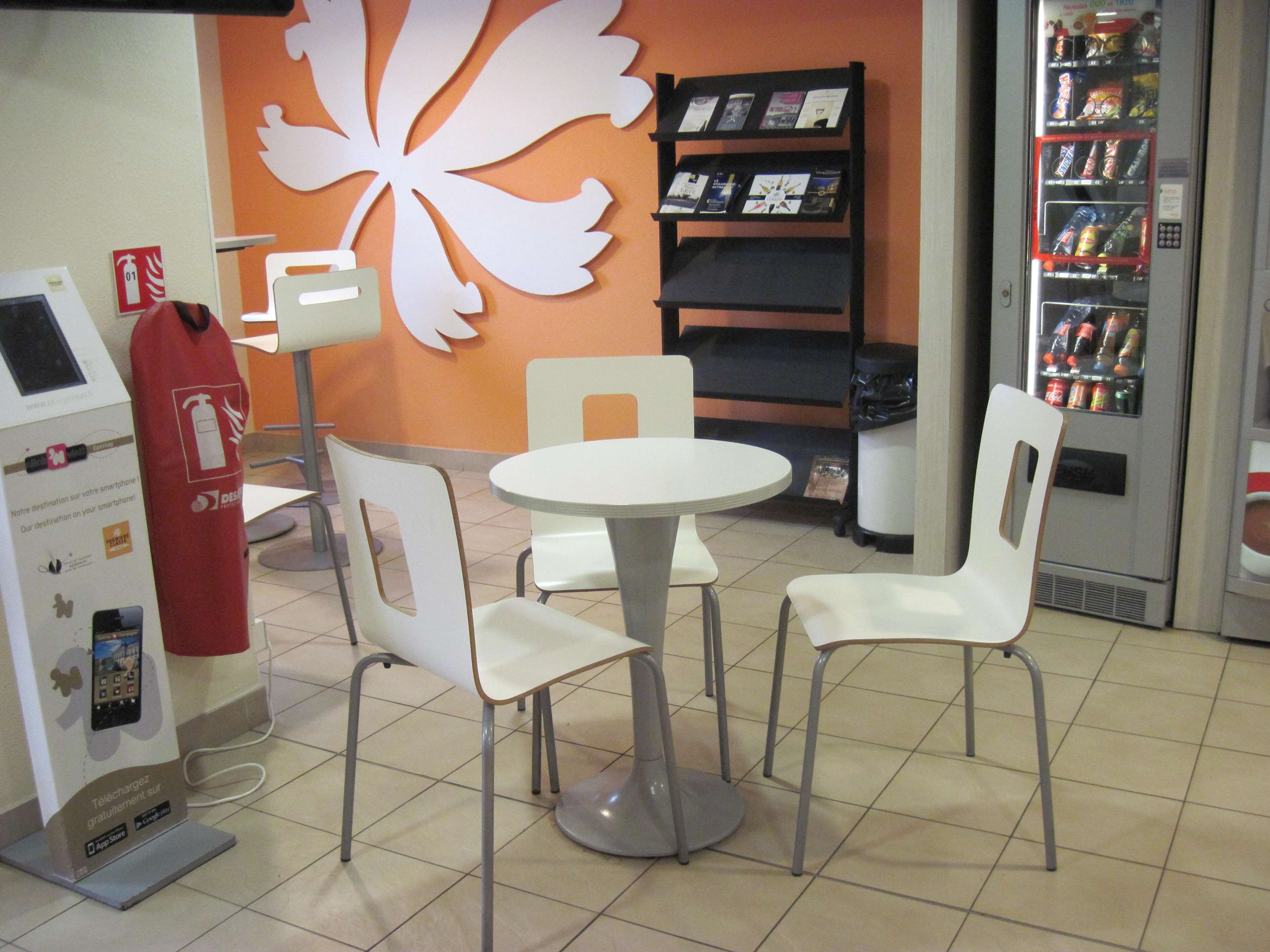 A small indoor seating area with a round table and four chairs, a bookshelf with books, a vending machine, and a fire extinguisher.