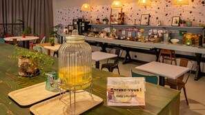 A bar area with a glass jar of a yellow drink, a sign reading "Eau infusée Help yourself", and a green plant on a wooden table. - Greet Hotel Castres Saïx (Saix)