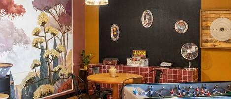 A room with a foosball table, a table with chairs, a wall with decorative plates, and a mural.