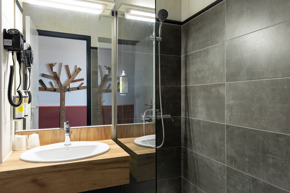 A bathroom with a wooden vanity, a sink, a mirror, and a shower area.