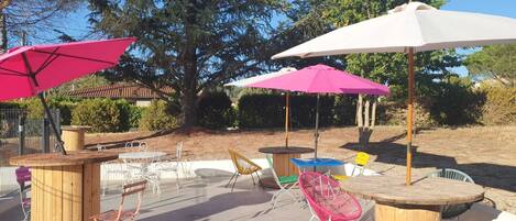 An outdoor seating area with round wooden tables and chairs, surrounded by large umbrellas.