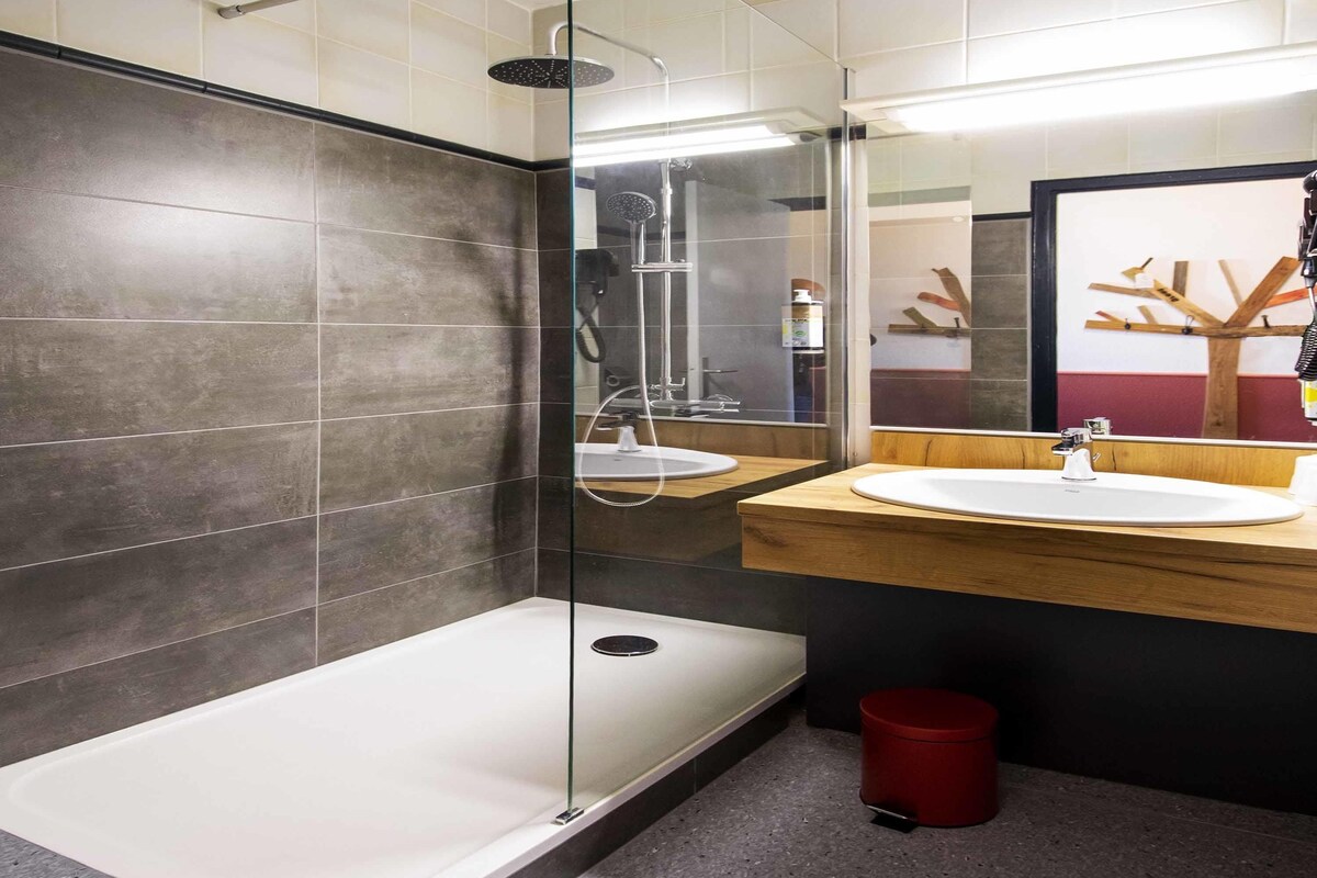 A modern bathroom with a glass-enclosed shower, two sinks with wooden countertops, and a red trash bin.