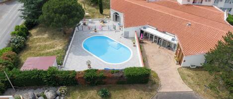 An aerial view of a hotel with a swimming pool, a covered patio, and a red-tiled roof.