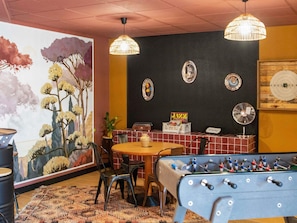 Um quarto com mesa de pebolim, uma mesa com cadeiras, parede com pratos decorativos e um mural.