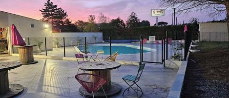 Un espace piscine avec une piscine entourée d’une clôture, des sièges extérieurs et une enseigne « Greet Hotel ».