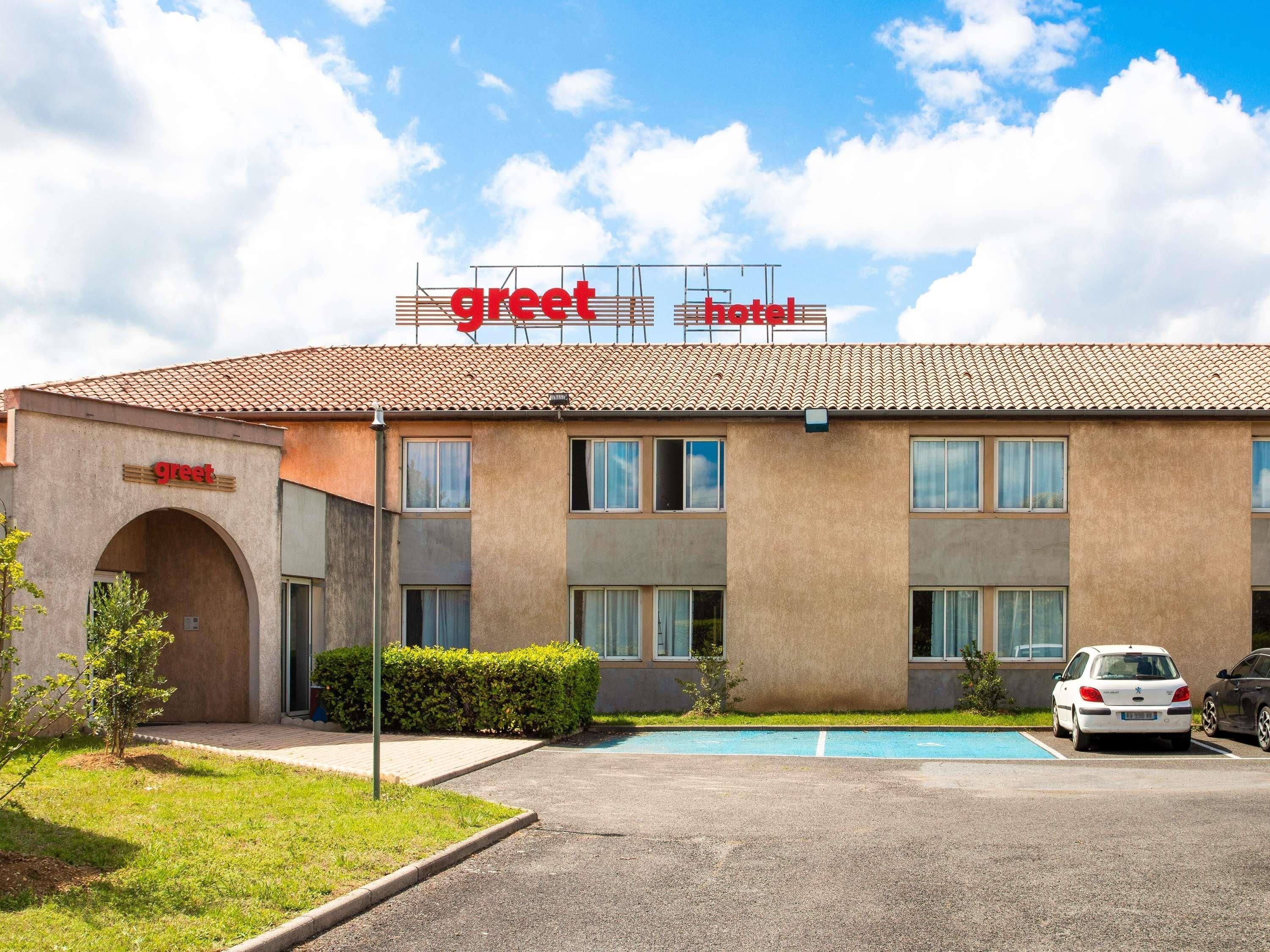 A two-story building with a 'greet hotel' sign, a parking lot, and a swimming pool.