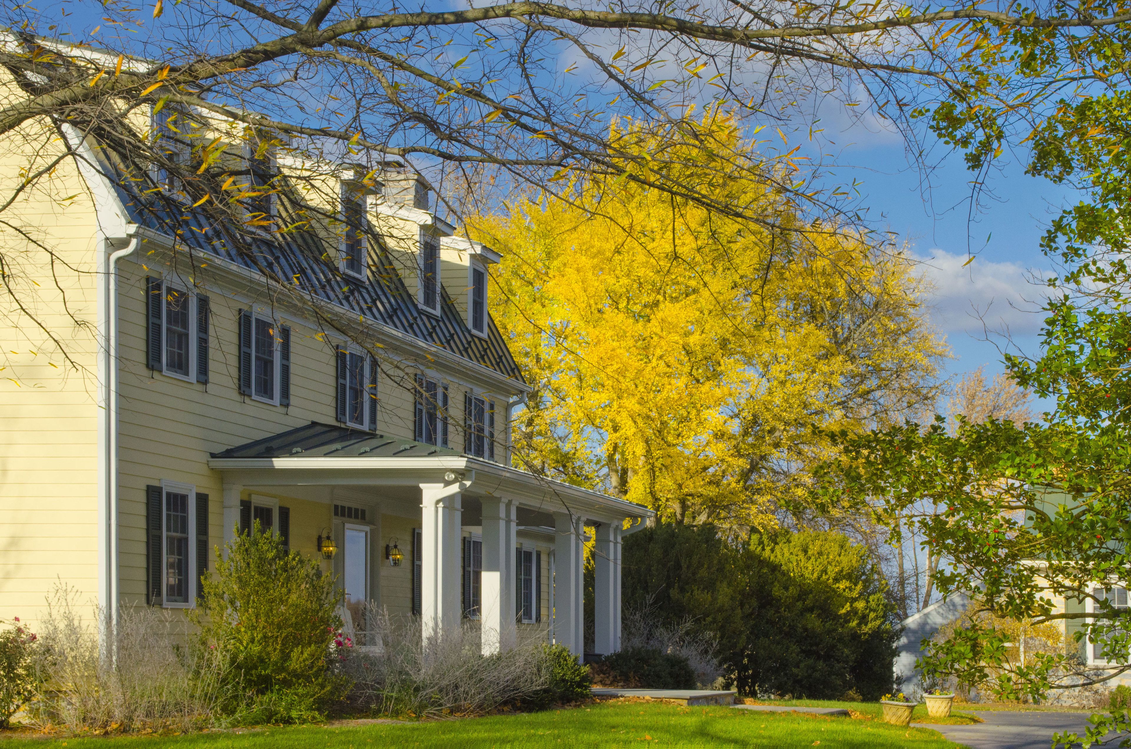 A two-story house with a porch, surrounded by trees with yellow leaves.