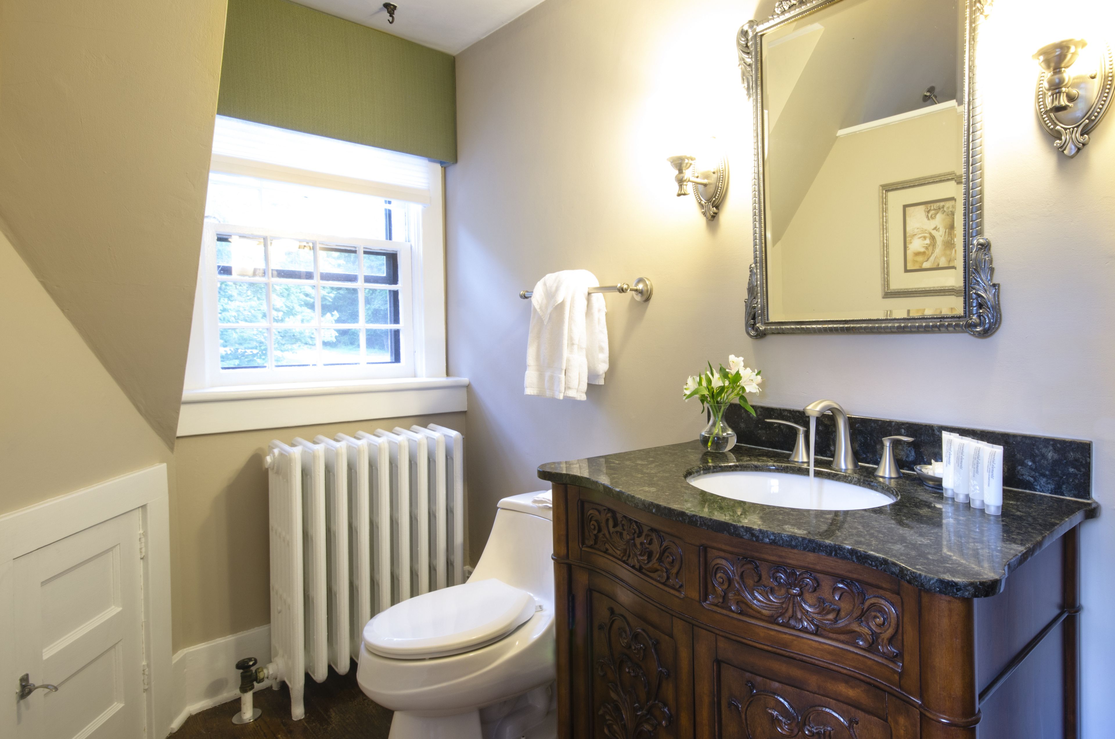 A bathroom with a white toilet, a radiator, a vanity with a marble countertop, and a large mirror.