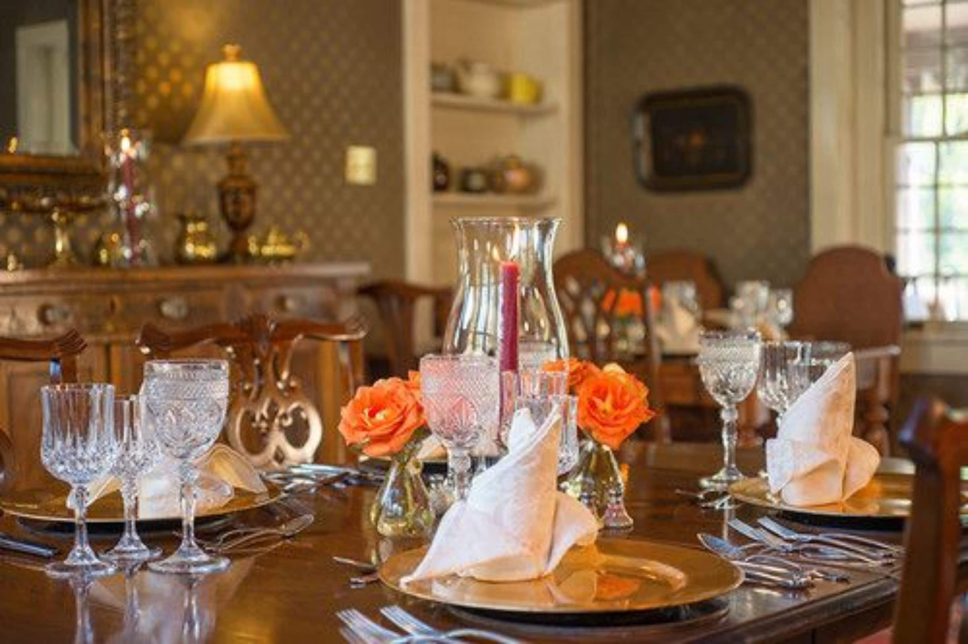 Una mesa de comedor adornada con copas de cristal, un candelabro con flores anaranjadas.