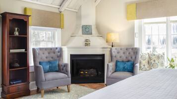 Une pièce chaleureuse avec une cheminée, deux fauteuils, un grand lit et une bibliothèque en bois.