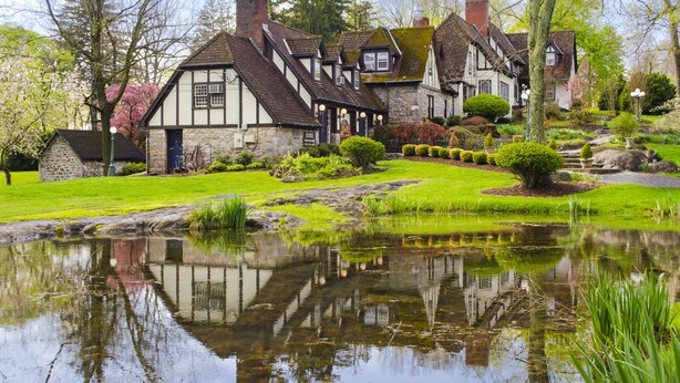 A traditional Tudor-style house with a pond in the foreground, surrounded by well-maintained gardens and trees. - Hillbrook Inn (Charles Town)