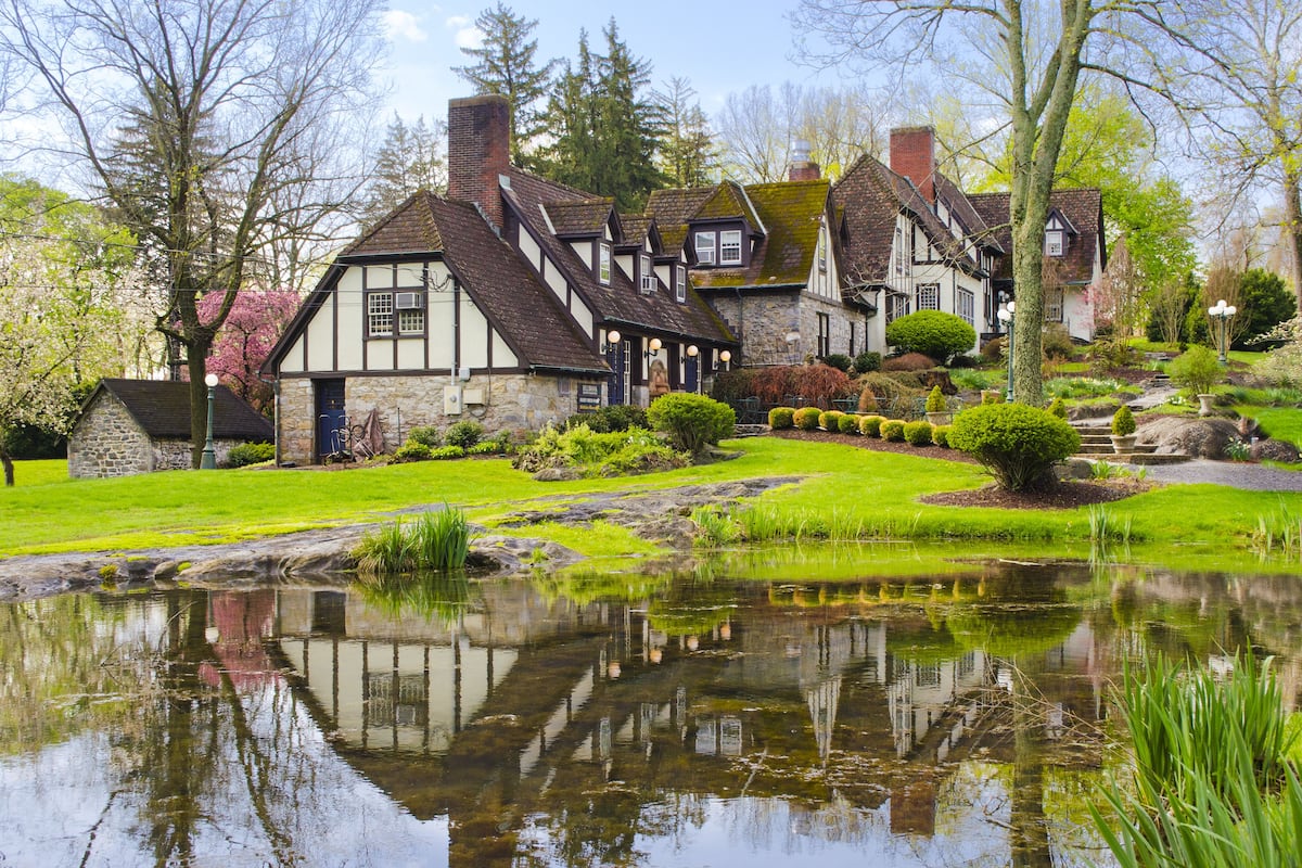 Ein traditionelles Haus im Tudor-Stil mit einem Teich im Vordergrund, umgeben von gepflegten Gärten und Bäumen.