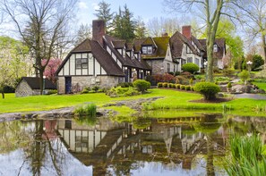 A traditional Tudor-style house with a pond in the foreground, surrounded by well-maintained gardens and trees. - Hillbrook Inn (Charles Town)