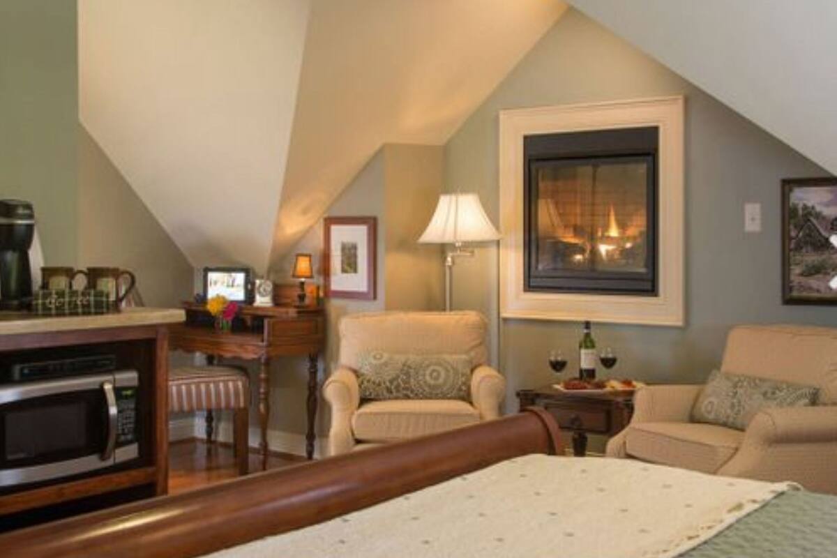 Ein gemütliches Zimmer mit einem Bett, zwei Sesseln, einem kleinen Tisch mit einer Lampe, einer Kaffeemaschine und einem gerahmten Bild an der Wand.