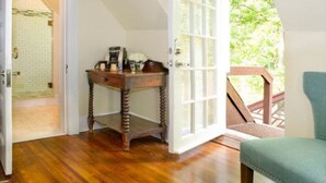 A room with a wooden floor, a small wooden table with a coffee maker, a chair, and a door leading to a balcony with a wooden railing. - Hillbrook Inn (Charles Town)