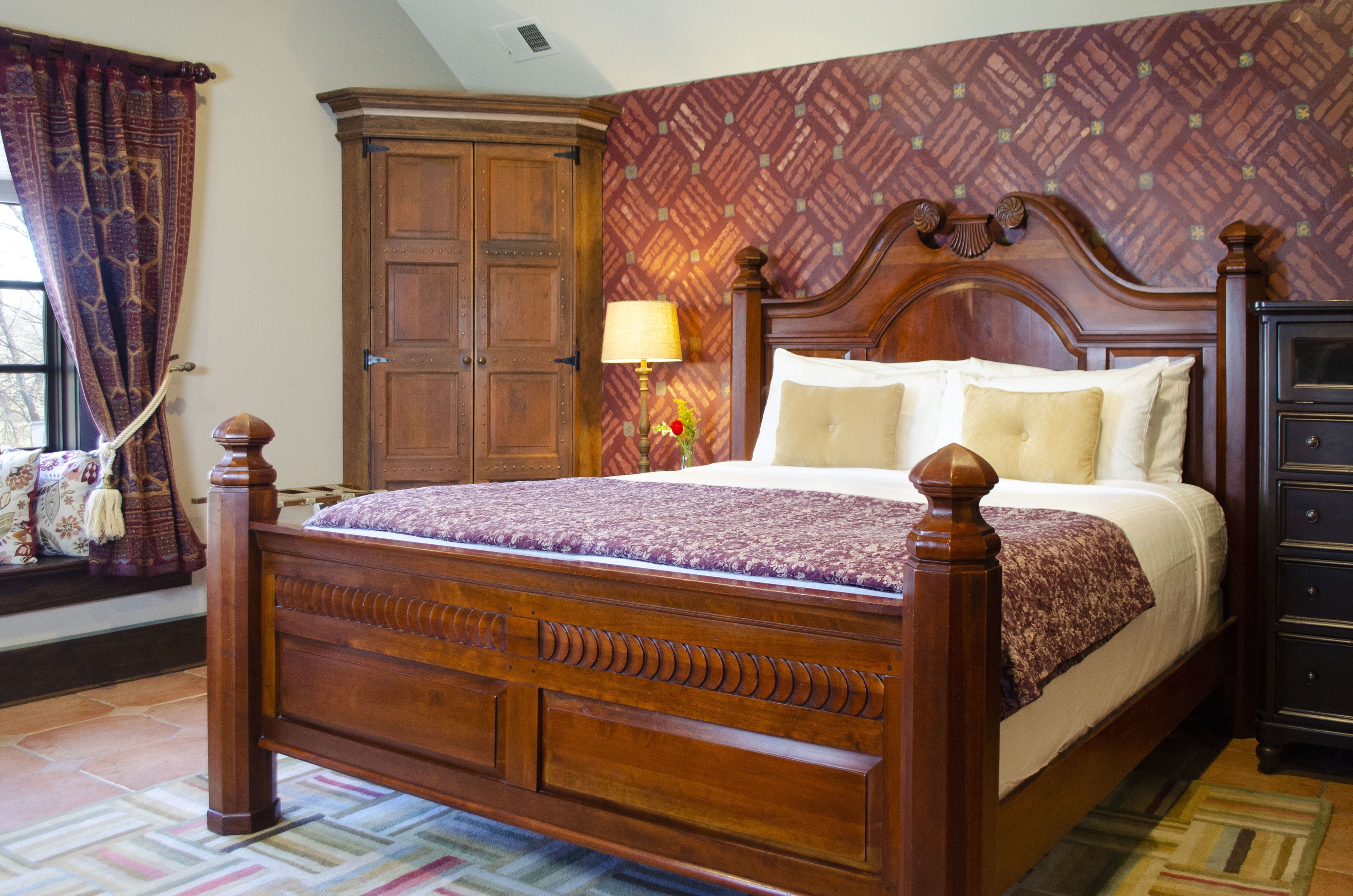 Un lit à baldaquin en bois, surmonté d’une couvre-lit à motifs, une table de chevet avec une lampe et une armoire.