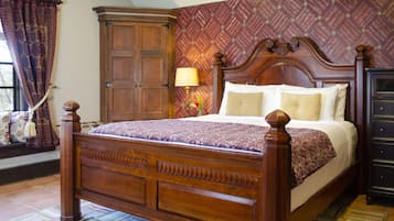 Un lit à baldaquin en bois, surmonté d’une couvre-lit à motifs, une table de chevet avec une lampe et une armoire.