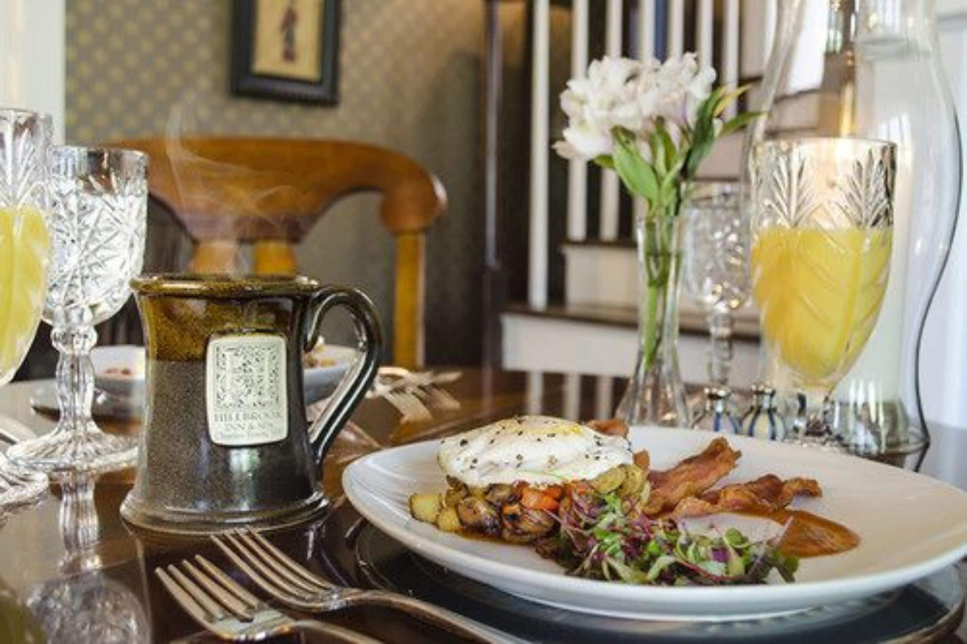 Une table mise pour le petit-déjeuner, avec une assiette de nourriture, une cafetière et des verres de jus d’orange.