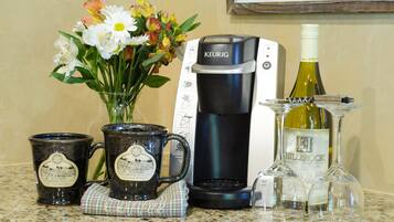 A coffee maker, two mugs, a vase with flowers, and a wine bottle on a kitchen counter.