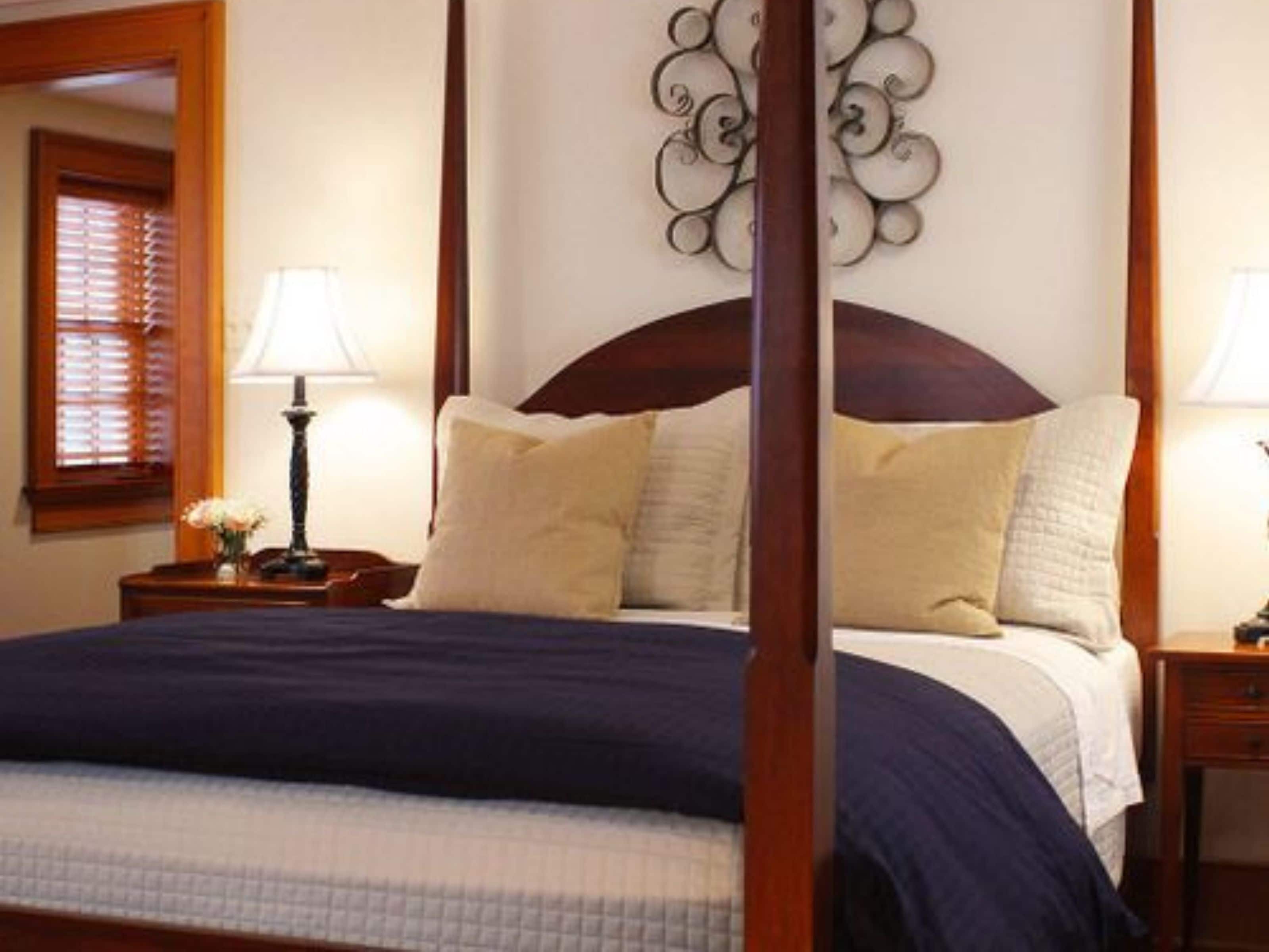 A neatly made bed with a dark blue bedspread and white pillows, flanked by wooden nightstands with lamps.