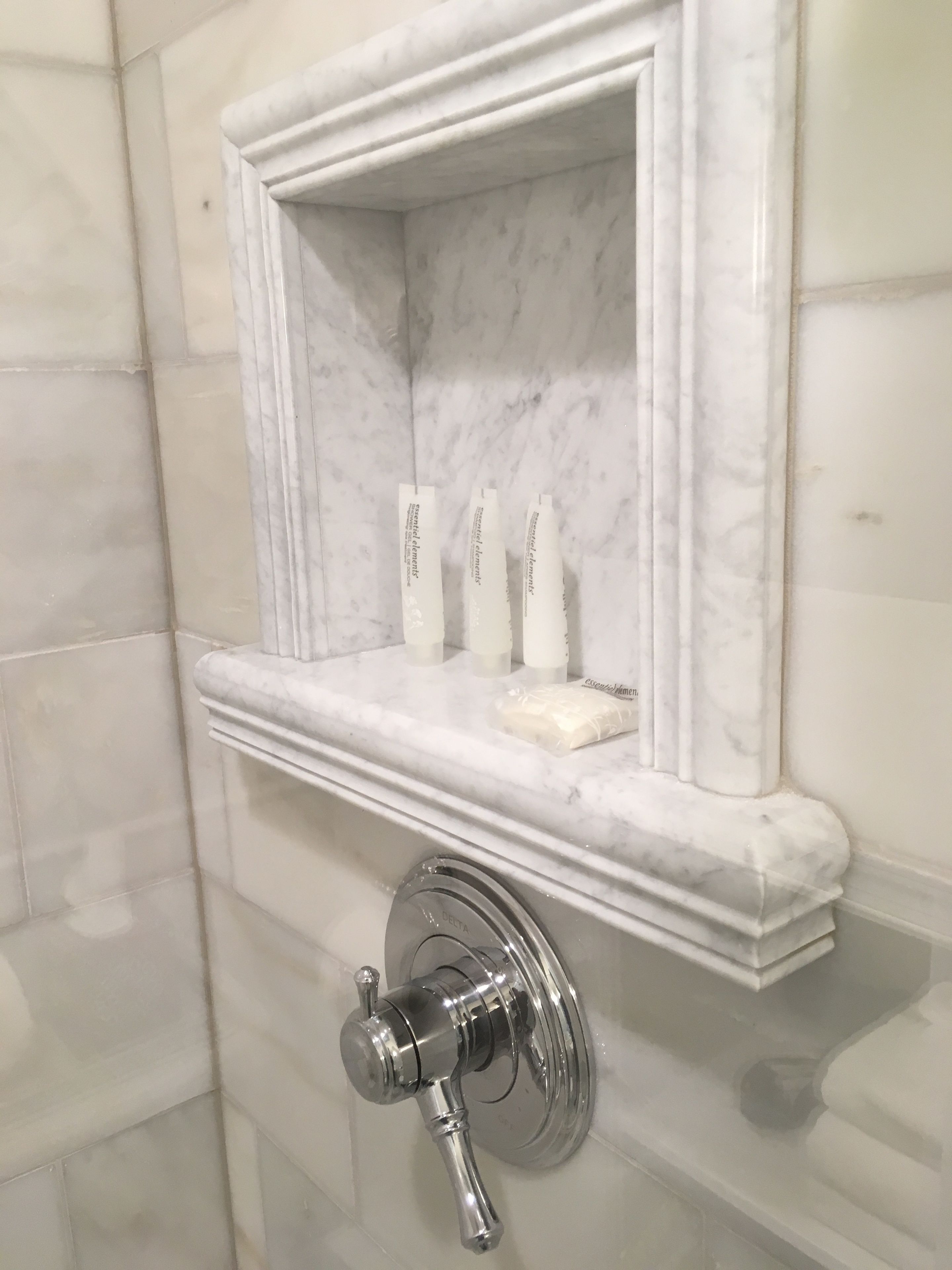 A bathroom with a marble shelf holding toiletries and a Delta showerhead.