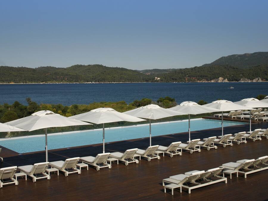 A poolside area with lounge chairs and umbrellas, overlooking a body of water and hills.