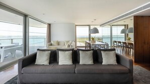 Una sala de estar moderna con sofá, comedor y ventanas amplias con vista a un cuerpo de agua.