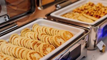 A buffet with various food items, including pancakes and waffles, served in metal trays.