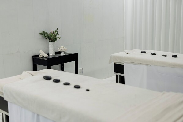Un cuarto de tratamientos de spa con una camilla de masaje, una mesita con un florero y una camilla de masaje montada en la pared.