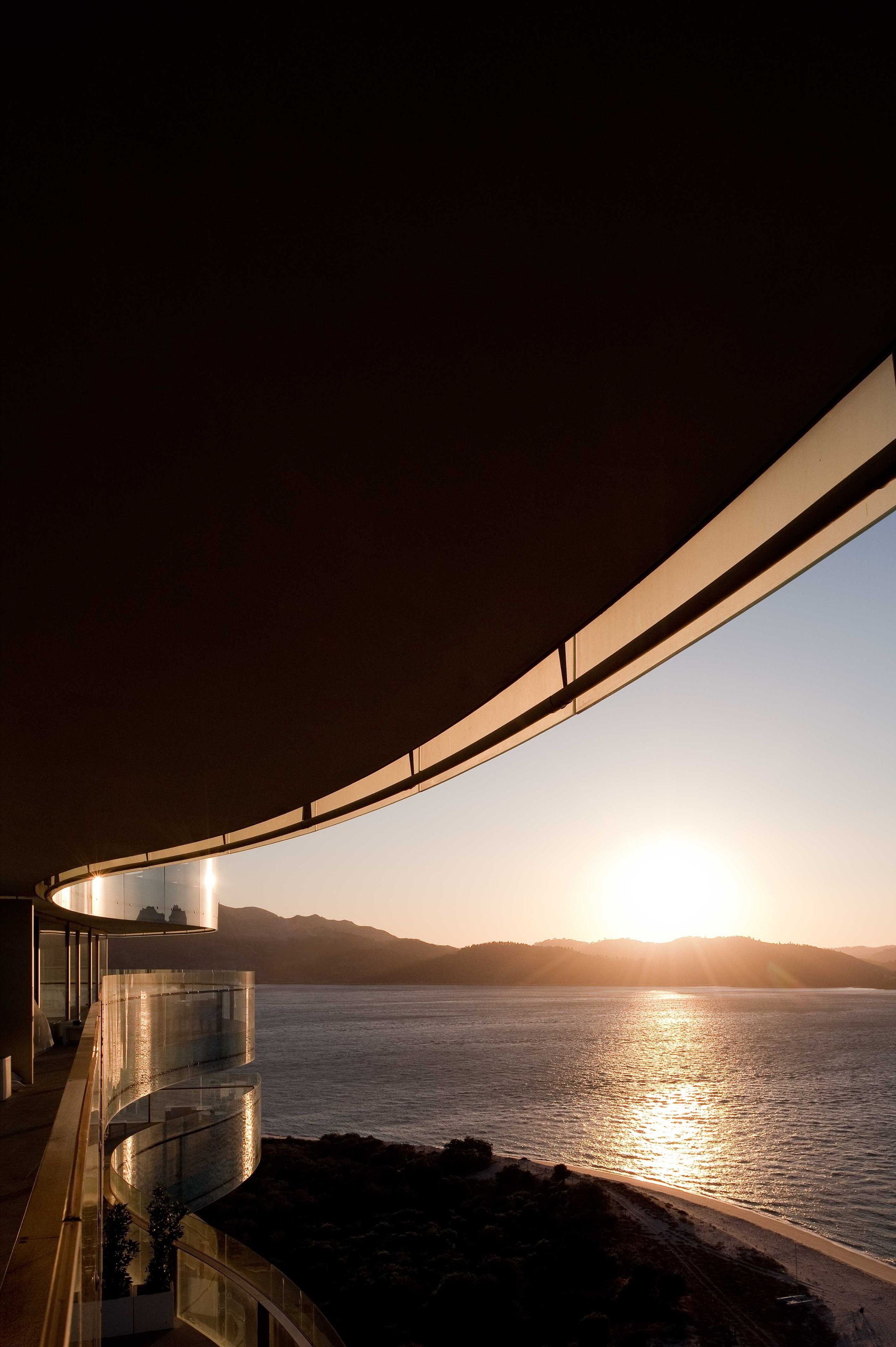 Un edificio moderno con un balcón curvo que da a una playa al atardecer.