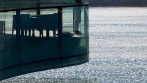 Un balcón con paredes de vidrio que ofrece vistas a un cuerpo de agua y una montaña al fondo.